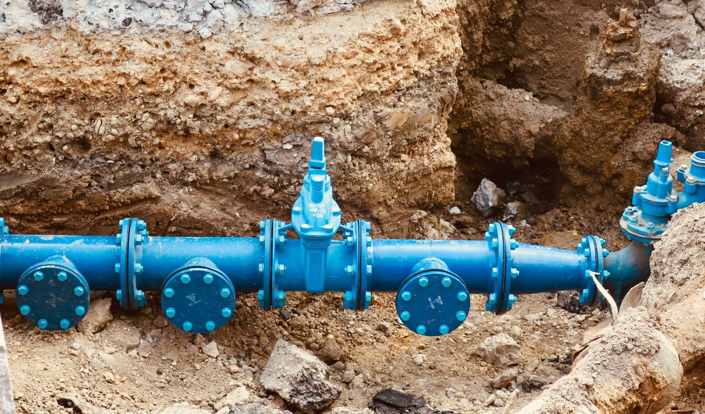Blue water-main pipe and valves in an excavated trench